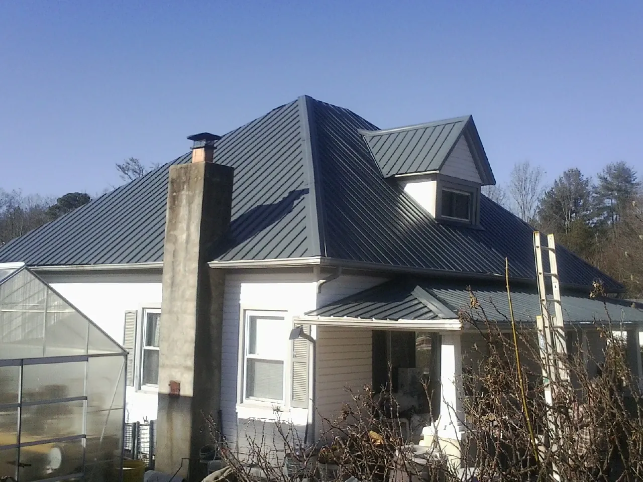 Dark blue standing seam metal roof on a white farmhouse with dormer — Slate & Tile Roof Repair by Roofing Brothers in Walton