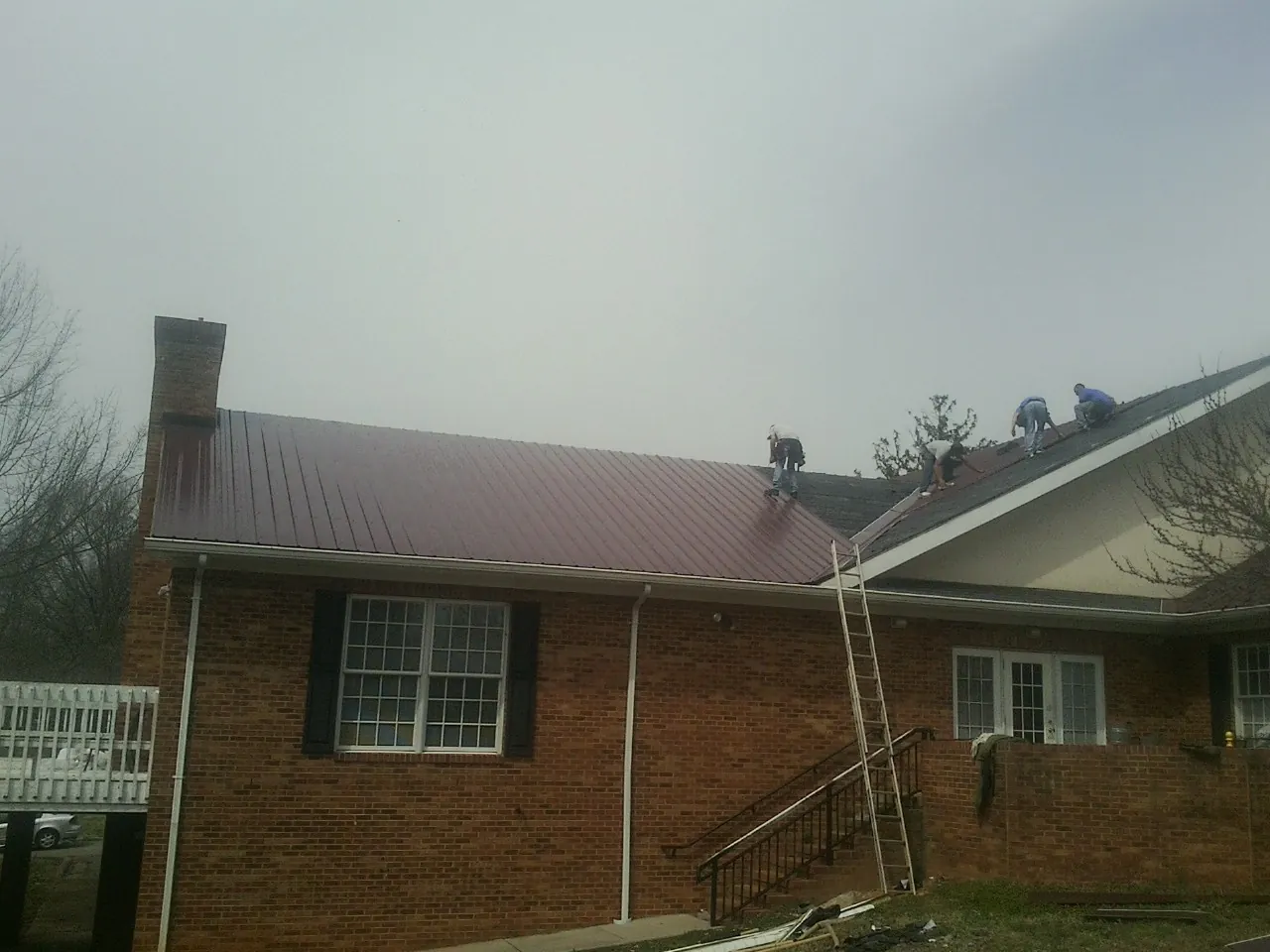 Crew setting red metal roofing panels on a brick home in Walton