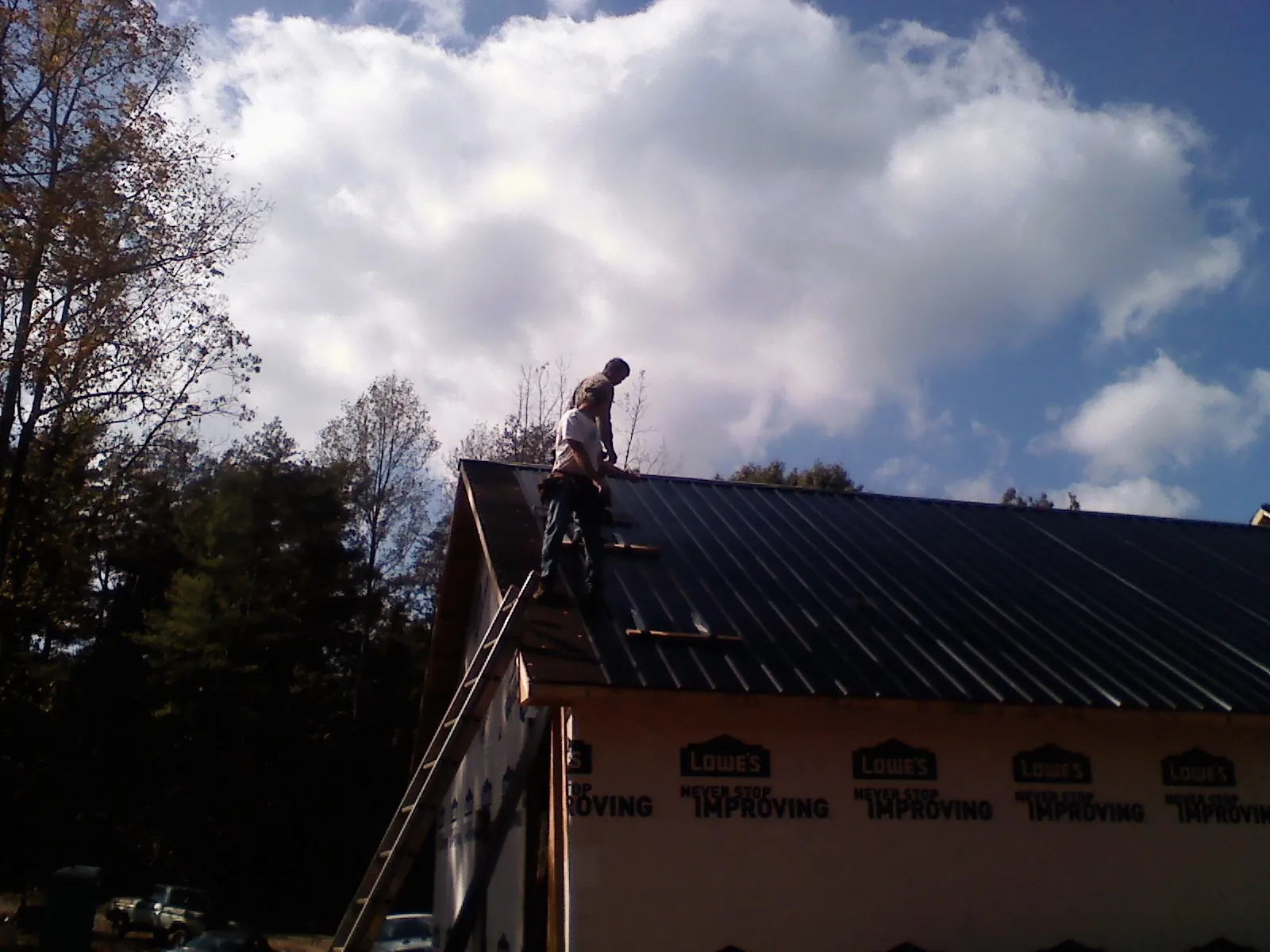 Roofer fastening dark metal panels high against a cloudy sky, from a Roof Inspection job in Walton